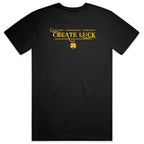 A black short-sleeve crewneck t-shirt with a gold graphic on the back reading 'CREATE LUCK' and 'HARD WORK + PREPARATION + OPPORTUNITY' above it, accompanied by a small four-leaf clover symbol, shown on a plain black background.